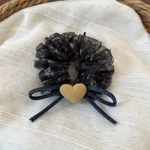 Dettaglio dell'elastico per capelli in rete floreale, fiocco in denim e ciondolo a cuore.