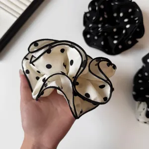 Dettaglio di un elegante elastico per capelli a pois bianchi e neri con bordo arricciato.