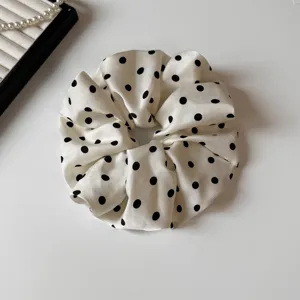 Dettaglio di scrunchie per capelli in raso a pois neri e bianchi elegante con tessuto morbido.
