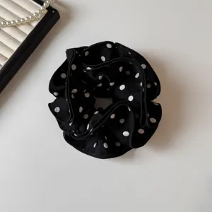 Vista dettagliata di un elastico per capelli nero a pois bianchi, tessuto morbido.