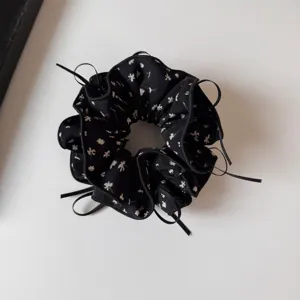 Close-up of black floral scrunchie with cute ribbons, soft fabric and pleated ruffled design.
