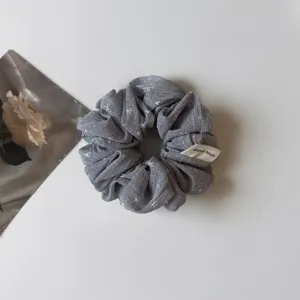 Primo piano dettagliato dello scrunchie per capelli grigio con stampa a fiocco e etichetta fatta a mano.