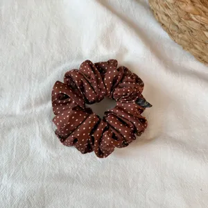 Detailed shot of brown polka dot hair scrunchie, smooth fabric with white dots, ruffles.