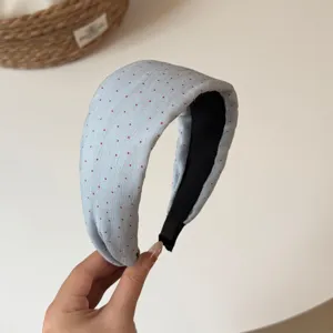 Close up view of light blue wide fabric headband with red polka dots and black inner lining design.