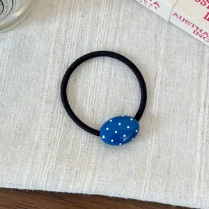 Primo piano di un elastico per capelli ovale blu a pois su lino, accessorio dolce.