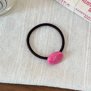 Dettaglio in primo piano dell'elastico per capelli rosa a pois su tessuto bianco.