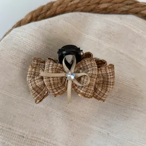 Primer plano del clip para el pelo con lazo a cuadros marrones, textura tweed y cristal.