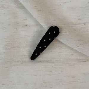 Detailed view of a black snap hair clip with white polka dots, fabric wrapped daily wear.