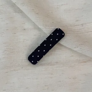 Close-up detail of a classic black polka dot hair clip, showing the fabric texture clearly.