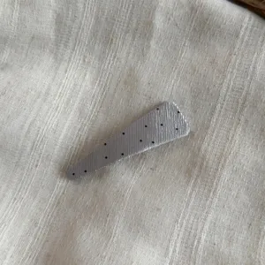 Detalle en primer plano de la pinza para el cabello BB de lunares texturizada gris con pliegues.