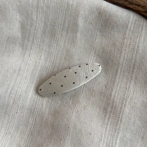 Primer plano de una pinza de pelo de tela con lunares en tela beige texturizada.