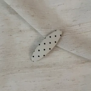 Close-up detail of a beige fabric hair clip with black polka dots, elegant fringe BB clip.