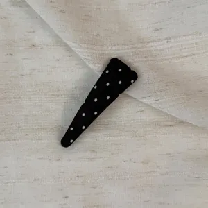 Detail shot of black polka dot hair clip on textured fabric, ideal for stylish daily hairstyles.
