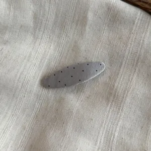 Primer plano de una pinza de pelo de tela plisada gris con topos negros, elegante.