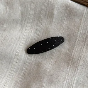Primer plano detallado de una pinza para el pelo de tela negra con lunares blancos.