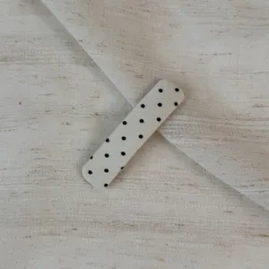 Detailed view of off-white fabric snap hair clip with cute black polka dot pattern design.