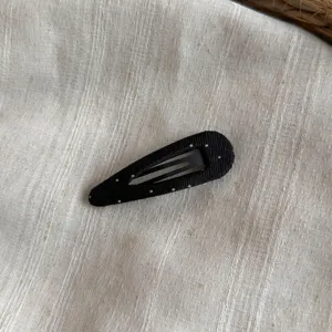 Primer plano detalle de horquilla negra de tela con lunares sobre fondo texturizado beis.