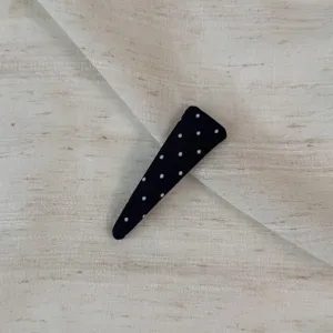 Detail close-up of a black polka dot fabric snap hair clip on textured beige fabric.