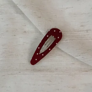 Close-up detail of a dark red polka dot snap hair clip with fabric wrap and metal base.