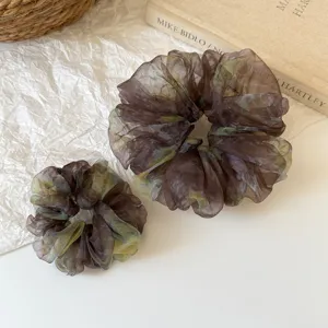 Detailed shot of brown tie-dye hair scrunchies set on white crumpled fabric backdrop.