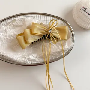 Close-up of gold satin bow hair clip with ribbons and rhinestone detail in a wire basket.