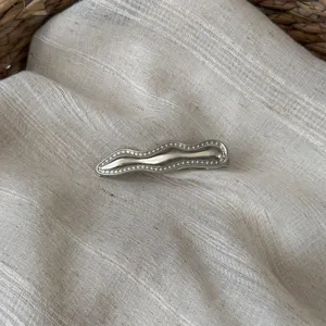 Detailaufnahme einer minimalistischen silbernen Wellen-Haarspange auf strukturiertem Stoff.