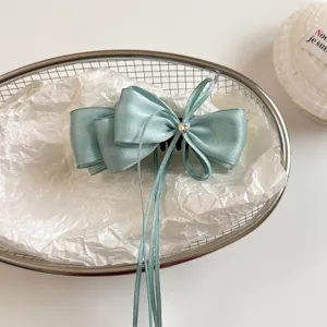 Detail shot of light blue satin bow hair clip with rhinestone and long ribbons in wire basket.