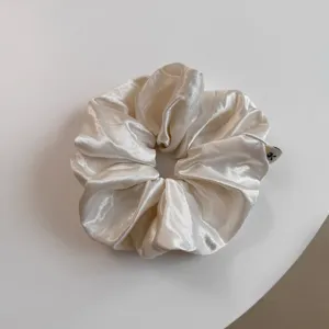 Gedetailleerd overzicht satijnen haarelastiek, elegante crèmekleur en glanzende textuur nabij.