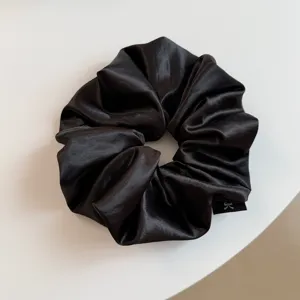 Detailopname van een klassieke zwarte satijnen haarelastiek, elegant glanzend haaraccessoire.