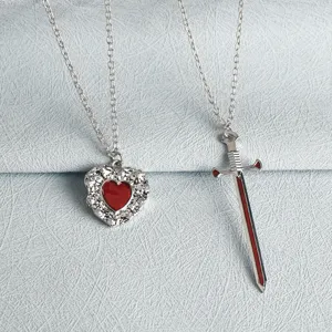Close-up of heart and sword pendant necklace set, detailed texture and red enamel finish.