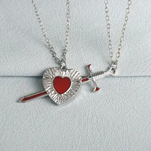 Detailed view of a silver heart pierced by a dagger necklace set, perfect couple jewelry gift.
