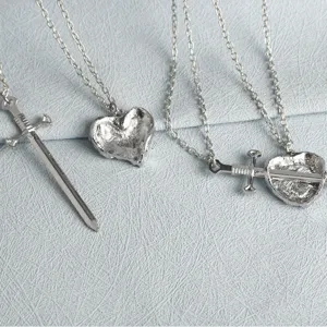 Detailed shot of silver heart and sword pendant necklace set, perfect for couples or friends.