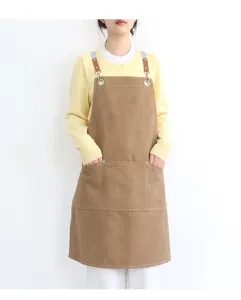 Detail shot of a brown canvas work apron with leather straps, metal rings and pockets.