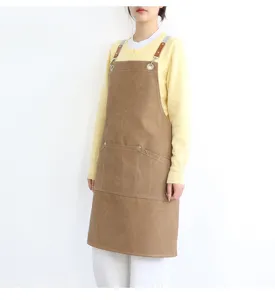 Detail view of a brown canvas apron with leather straps and metal rings, practical pockets.