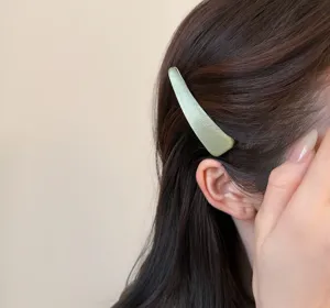 Primo piano di una forcina di raso verde chiaro su capelli castani, dettaglio elegante.