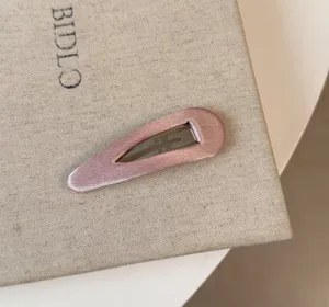 Primo piano fermaglio capelli raso rosa, superficie lucida e solida struttura metallica.