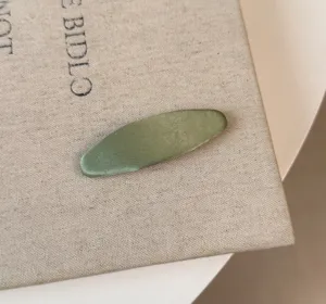 Vista dettagliata del fermaglio in satin verde, tessuto lucido e design minimalista.