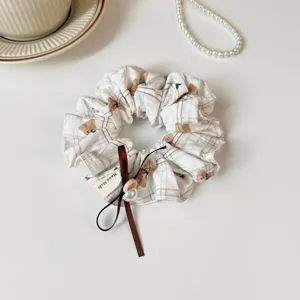 Detailed close up of cute plaid bear print hair scrunchie with brown ribbon and pearl for women daily use.