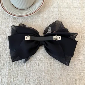 Vista dettagliata di una molletta per capelli a fiocco in organza nera, elegante accessorio.