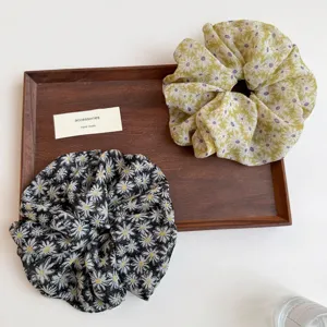 Detailed shot of pastoral daisy print hair scrunchies on a wooden tray, stylish hair accessories.