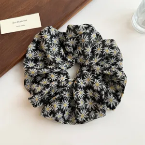 Close-up detail of black floral print hair scrunchie with cute white daisies, soft fabric design.