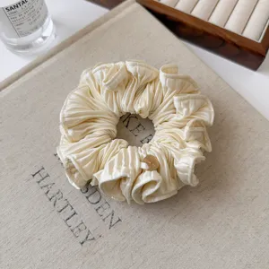 Elegantes plissiertes Haargummi in Cremeweiß mit goldenem Charm für stylische Frisuren.