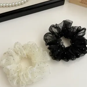 Close-up detail of black and white organza hair scrunchies with glittering dots on white surface.