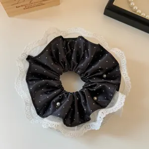 Close-up detail of black satin polka dot hair scrunchie with white lace trim and pearl accents.