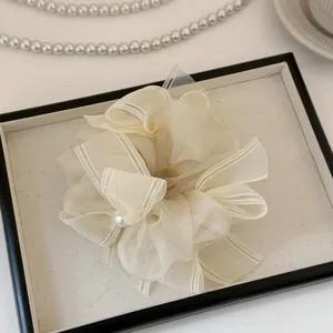 Détail d'un élégant chouchou en organza beige avec nœud ruban et détail de perle.