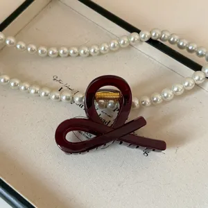 Primo piano dettaglio di molletta per capelli in acrilico rosso scuro con perle su vassoio.
