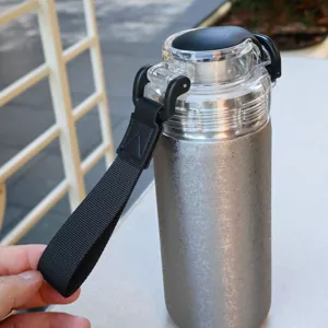 Stainless steel vacuum insulated water bottle detail featuring portable strap and clear lid.