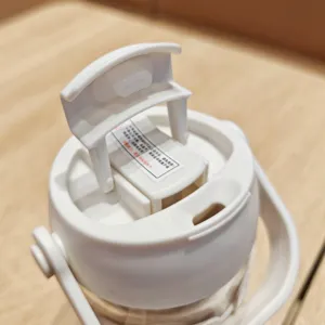 Detailed view of white plastic water bottle lid with portable handle and safety warning label.