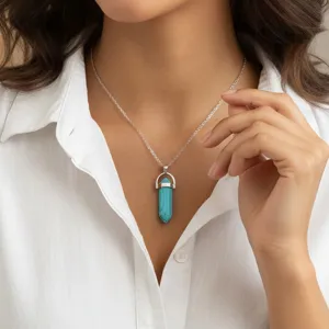 Close-up van een prachtige turquoise zeshoekige pilaar hanger ketting op wit shirt.