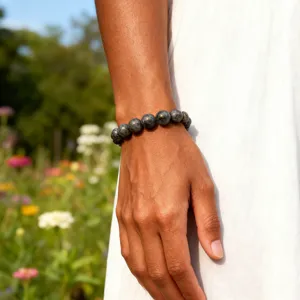 Detailaufnahme eines schwarzen Blitzstein Perlenarmbands am Handgelenk im blumigen Garten.